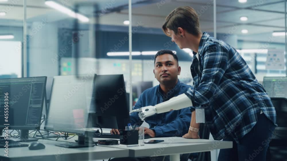 Teamwork In Diverse Inclusive Office: Woman with Disability Project Manager with Prosthetic Arm Talks with Indian Specialist Working on Desktop Computer. Professionals Software Engineers Create App