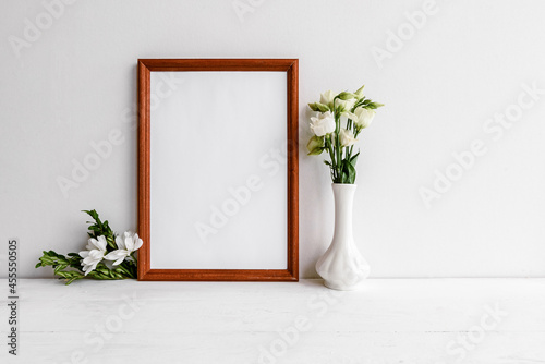 Fashionable female background on a white table - flowers and an empty photo frame. Wedding female background. Blank for a postcard.