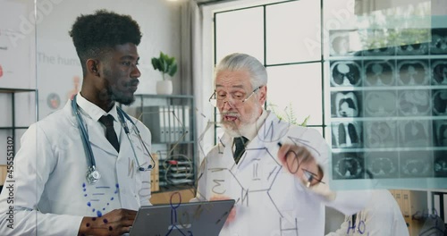 Attractive serious respected skilled bearded professor of medical university talking to his confident african american student in clinic lab and explaining x-ray scan photo