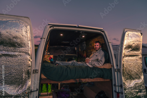 Fototapeta Caucasian guy from United Kingdom enjoying the sunset view from campervan