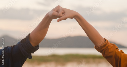 Young asia campers couple standing fist bump at campsite near beach. Happy male and female traveler success and fun when sunset in evening. Outdoor activity, adventure travel, or holiday vacation.