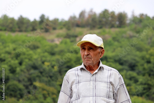 Portrait of elderly man on green mountain background. Life in village, travel in old age