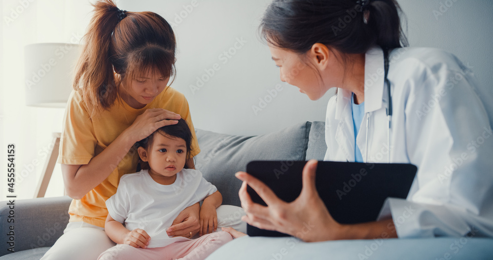 Φωτογραφία Young Asia female pediatrician doctor and little girl patient using digital tablet sharing good health test news with happy mom sit on couch in house