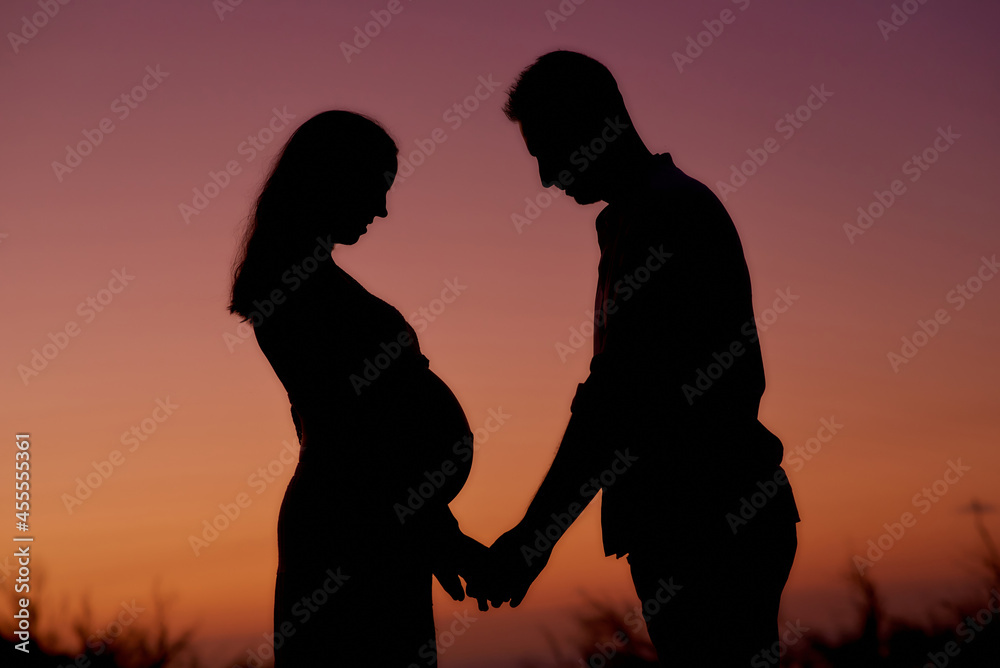 Couple expecting baby standing in sunset lights