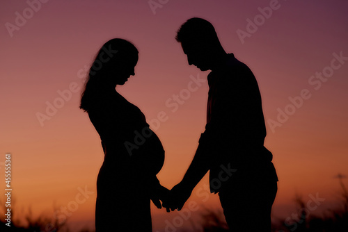 Couple expecting baby standing in sunset lights