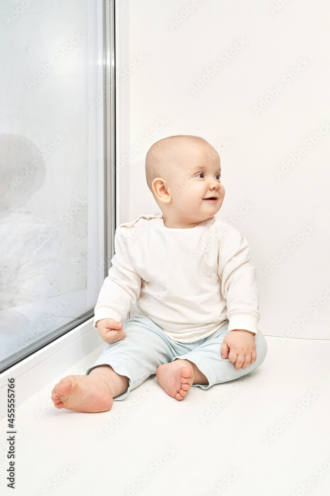 Cute small boy at house. Childhood concept. Light background. Smiling child. Happy emotion. Copyspace. Stay home. Onesie mockup. White clothes. Sitting on windowsill Cute small boy at house. Childhood concept. Light background. Smiling child. Happy emotion. Copyspace. Stay home. Onesie mockup. White clothes. Sitting on windowsill
