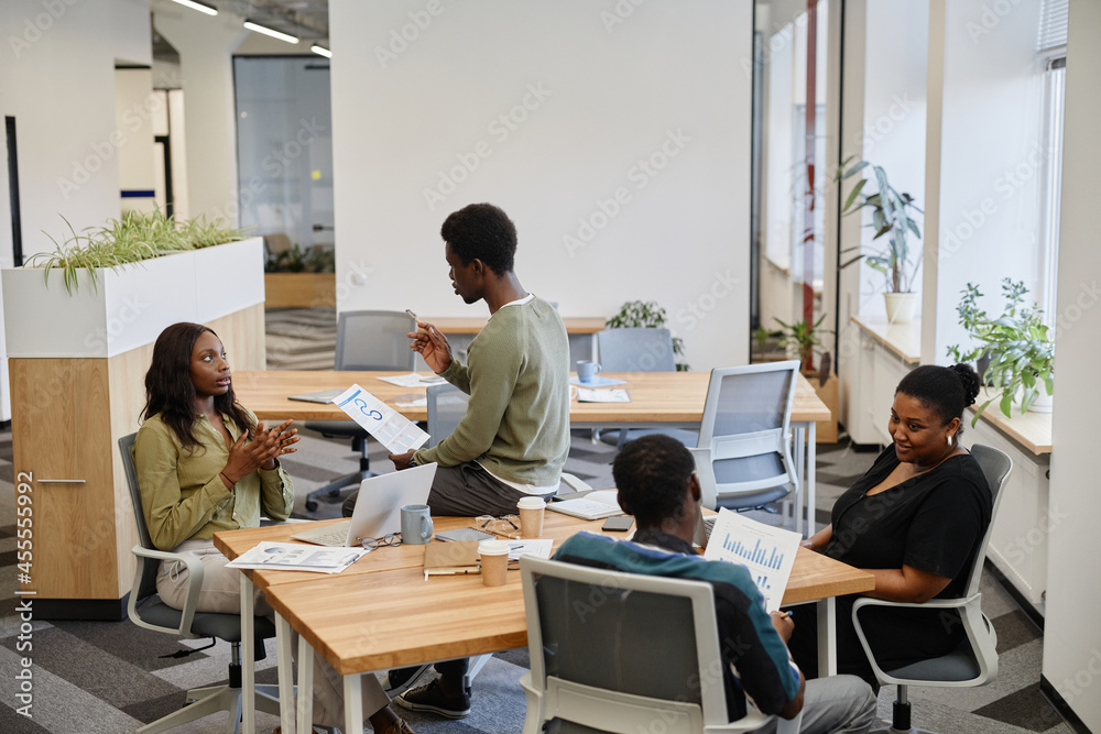 Business people working in open space office and discussing charts and reports with various sale and marketing data Business people working in open space office and discussing charts and reports with various sale and marketing data