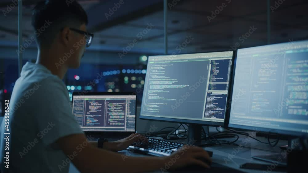 Night Office: Young Japanese Man in Working on Desktop Computer. Digital Entrepreneur Typing Code, Creating Modern Software, e-Commerce App Design, e-Business Programming. Over Shoulder