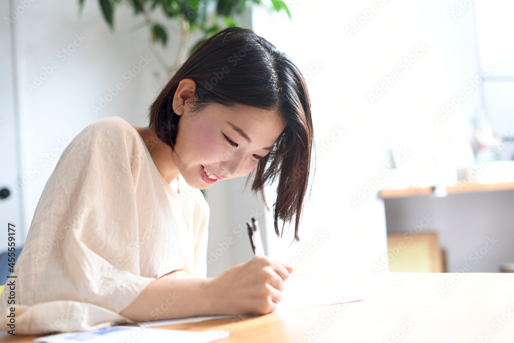 明るい室内でメモを書く私服の若い女性 明るい室内でメモを書く私服の若い女性