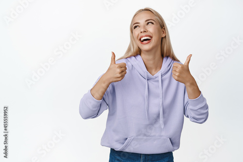 Glamour blond woman laughing, smiling and showing thumbs up, standing happy against white background