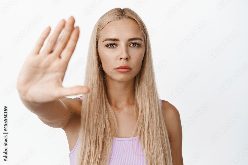 Confident young woman stretch out hand to show stop gesture, telling no, prohibit something, saying no, standing over white background Confident young woman stretch out hand to show stop gesture, telling no, prohibit something, saying no, standing over white background