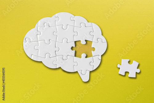 Brain shaped white jigsaw puzzle on yellow background, a missing piece of the brain puzzle, mental health and problems with memory