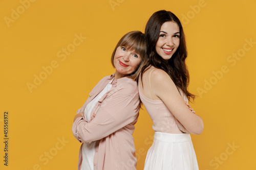 Side view two young fun daughter mother together couple women wear casual beige clothes standing back to back look camera isolated on plain yellow background studio portrait Family lifestyle concept.