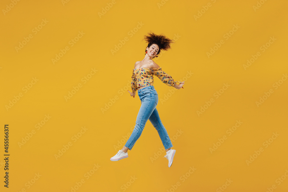Full length side view young happy smiling woman 20s with culry hair in casual clothes jump high show victory sign gesture isolated on plain yellow background studio portrait. People lifestyle concept. Full length side view young happy smiling woman 20s with culry hair in casual clothes jump high show victory sign gesture isolated on plain yellow background studio portrait. People lifestyle concept.