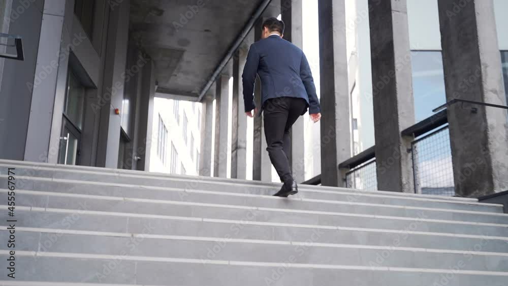 young successful and confident asian business man fast climbs the stairs up. going modern office building outside. Rear view back. Male businessman executive in formal suit goes to meeting in downtown