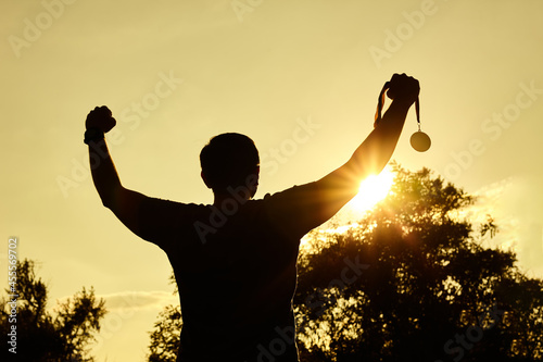 Silhouette people victory raising hands and holding gold medal with sunset sky.