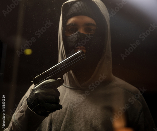 Armed criminal with balaclava holds gun in leather gloved hand. Shooting, killing, violence.