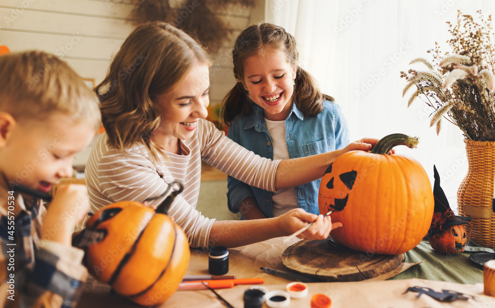 Fototapeta premium Smiling mother with children creating jack-o-lantern during Halloween celebration at home