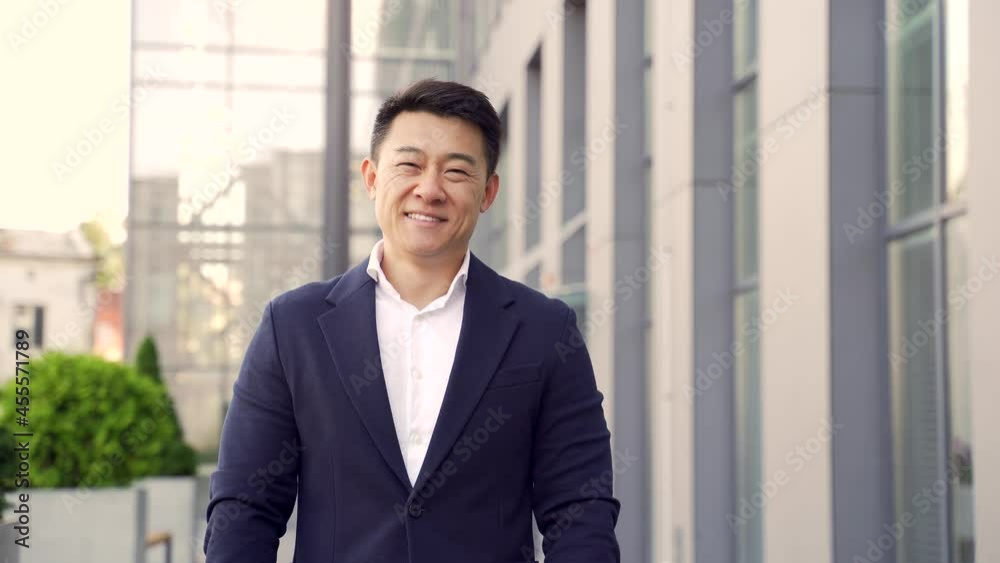 portrait of a young confident successful asian businessman looking at camera. Happy business man, close up smile standing on urban background of modern office building outdoors. Male in a formal suit portrait of a young confident successful asian businessman looking at camera. Happy business man, close up smile standing on urban background of modern office building outdoors. Male in a formal suit