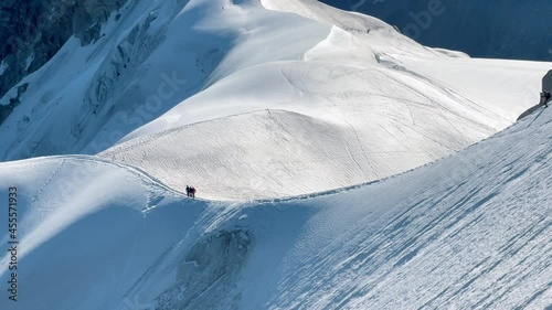 4K French Alps mountains peaks panorama view with climbers silhouettes as roping team descending on the snowy slope under Aiguille du Midi 3842m. Beauty of Nature and extreme people activity concept photo