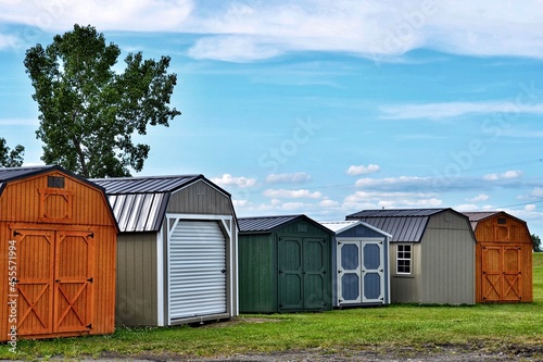 Various styles of wooden sheds on display. American shed is typically a simple, single-story roofed structure in a back garden or on an allotment that is used for storage, hobbies, or as a workshop. photo