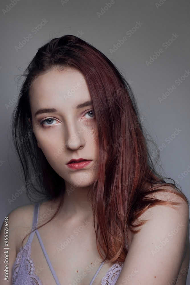 Portrait of a gentle serious gray-eyed girl on a gray background. Perfect porcelain skin. Long chic hair. Expressive look 