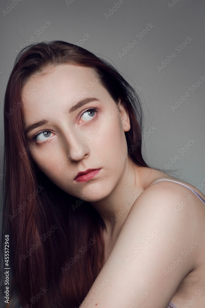 Portrait of a gentle serious gray-eyed girl on a gray background. Perfect porcelain skin. Long chic hair. Expressive look Portrait of a gentle serious gray-eyed girl on a gray background. Perfect porcelain skin. Long chic hair. Expressive look