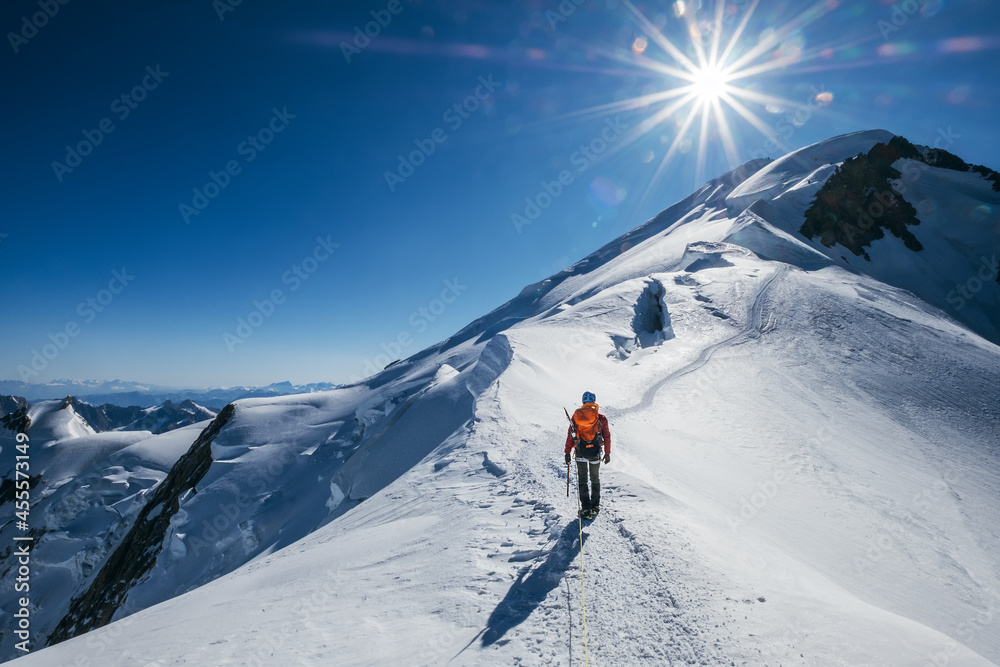Before Mont Blanc (Monte Bianco) summit 4808m last ascending. Team roping up Man with climbing axe dressed high altitude mountaineering clothes with backpack walking by snowy slopes with blue sky. - obrazy, fototapety, plakaty 