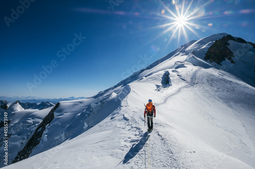 Before Mont Blanc (Monte Bianco) summit 4808m last ascending. Team roping up Man with climbing axe dressed high altitude mountaineering clothes with backpack walking by snowy slopes with blue sky. photo