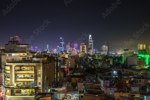 View of the Ho Chi Minh from rooftop bar at night with bright towers in the distance and poor disctrict in front photo