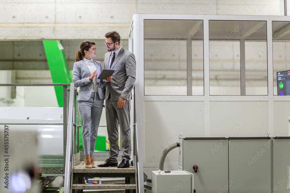 Factory management. Businesspeople checks the condition of the machine for automatic washing of apples. Man and a woman in a suit stand on the stairs and monitor the process while holding a tablet
