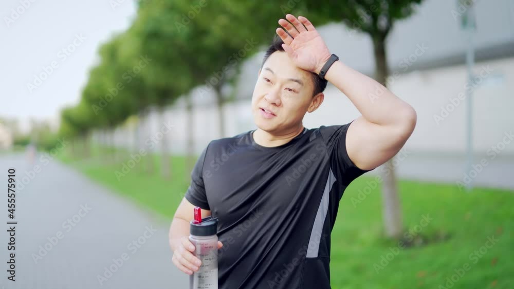 Tired exhausted dehydrated Athlete man runner drinking water bottle after workout. Sports bottle drink sport male drink. Asian runner sweaty and thirsty after difficult jogging outdoors in city park Tired exhausted dehydrated Athlete man runner drinking water bottle after workout. Sports bottle drink sport male drink. Asian runner sweaty and thirsty after difficult jogging outdoors in city park