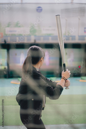 Back view of woman about to hit the ball with baseball bat