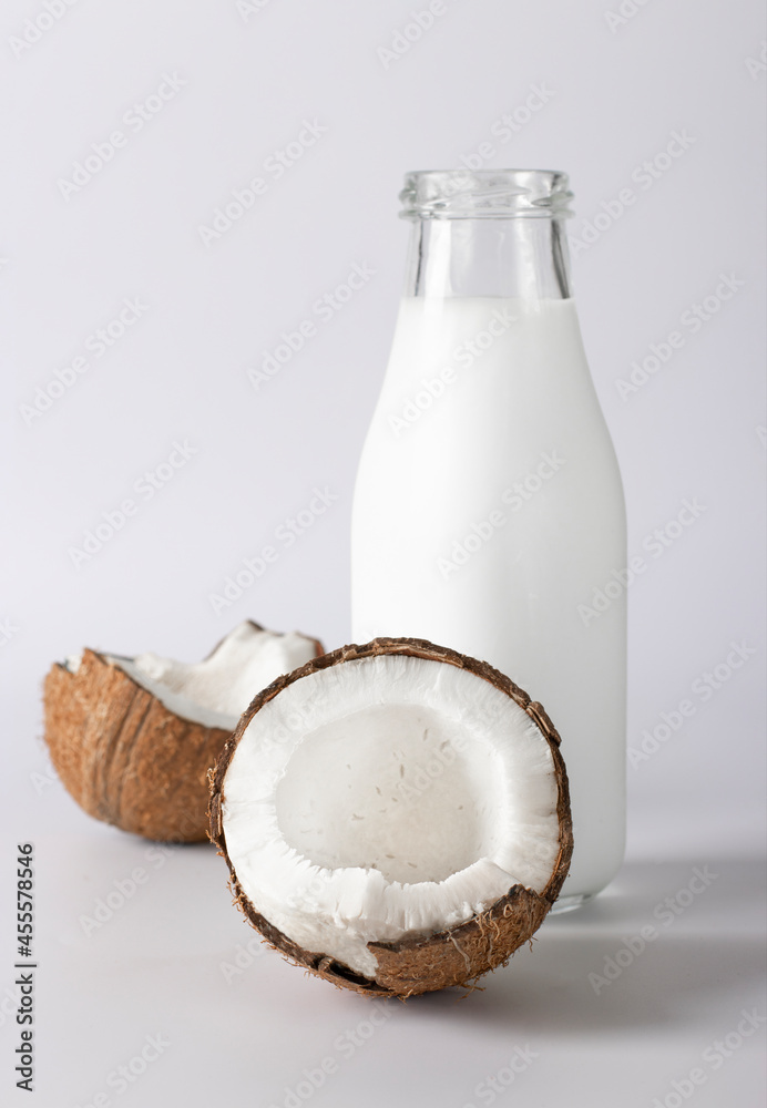 Coconut milk in a bottle and fresh coconut on a white background. Vegetarian food. Vertical format Coconut milk in a bottle and fresh coconut on a white background. Vegetarian food. Vertical format