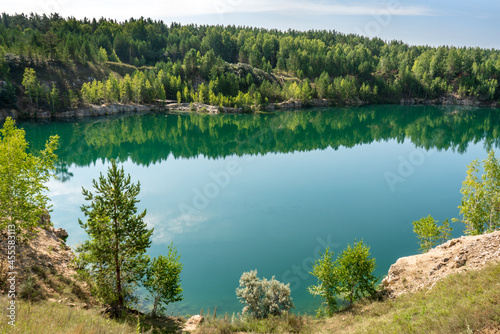 Turquoise lake in the middle of rocky shores and forest with reflective sky and clouds.