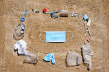 Medical mask on the beach with rubbish as a symbol of nature protection from pollution. Environmental protection concept.