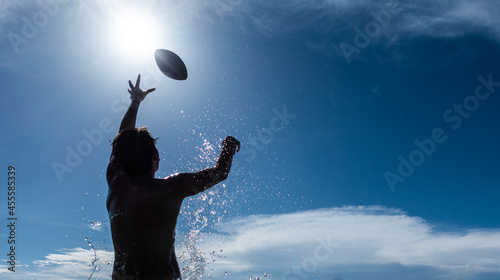 Silhouette of a man in body of water throwing an American football under blue sky photo