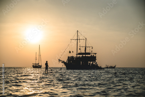 Silhouette of man near sail boat and a ship during sunset