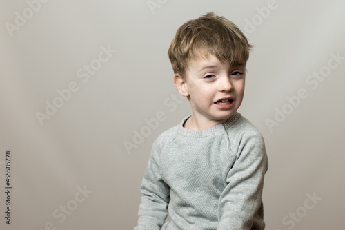 little boy of European appearance with a sad face. the baby is crying. gray background. emotions