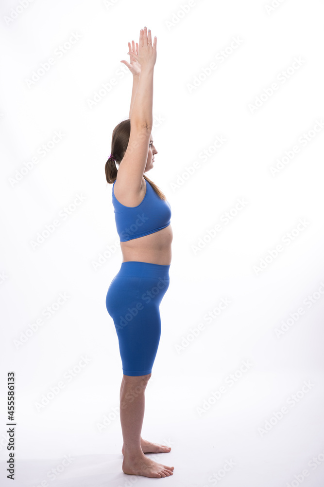 a girl of European appearance in a blue suit is engaged in fitness or yoga. White background. not a perfect figure. Athletic training. Hands up. vertical photography. side view. a girl of European appearance in a blue suit is engaged in fitness or yoga. White background. not a perfect figure. Athletic training. Hands up. vertical photography. side view.