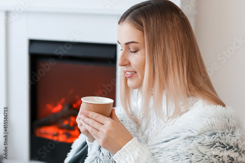 Young woman drinking hot tea near fireplace at home