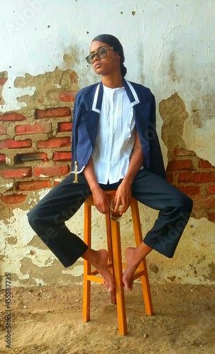 Woman in blazer and sunglasses sitting on stool indoor photo