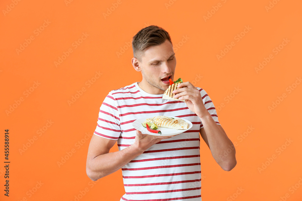 Young man eating tasty quesadilla on color background Young man eating tasty quesadilla on color background
