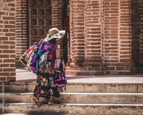 Woman wearing colorful Chiapas dress holding bags climbing concrete stair outdoor photo