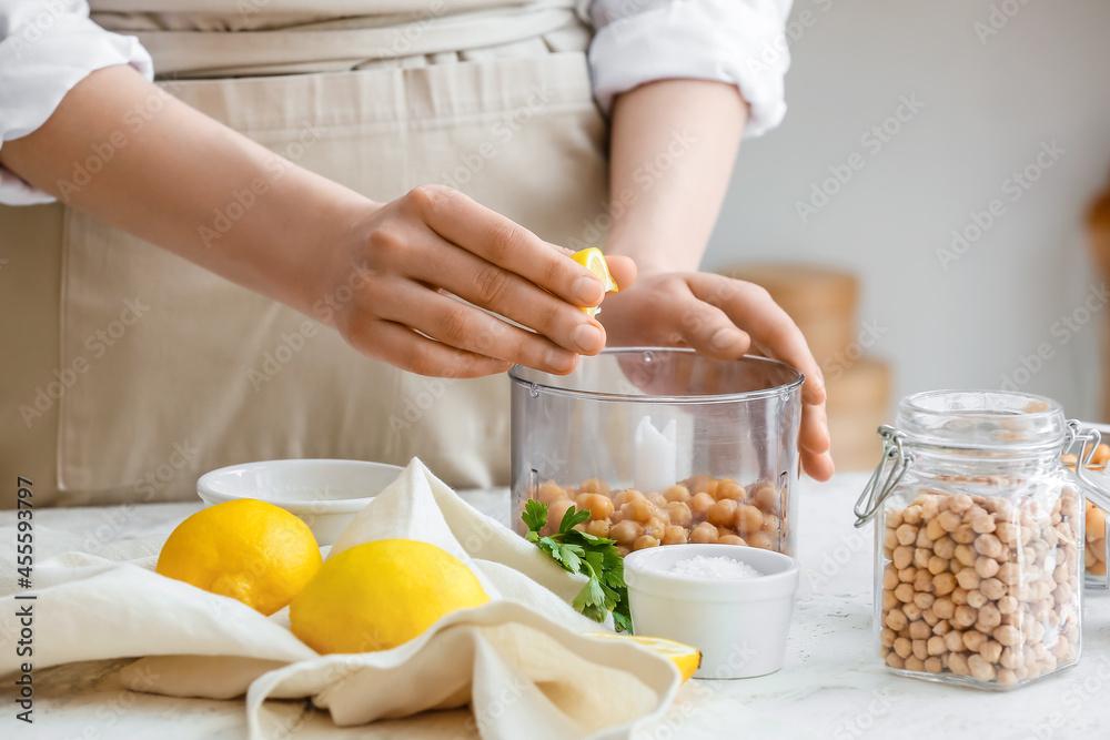 Woman squeezing lemon into blender with chickpeas on table in kitchen, closeup Woman squeezing lemon into blender with chickpeas on table in kitchen, closeup