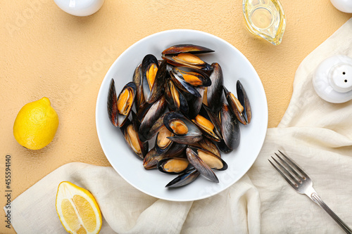 Bowl with tasty mussels and lemon on color background photo