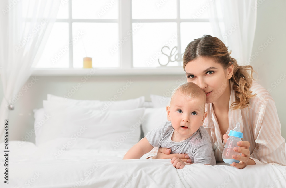 Young mother with little baby and bottle of water in bedroom