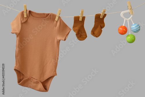 Baby clothes and toy hanging on rope against grey background photo