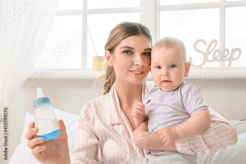 Young mother with little baby and bottle of water in bedroom