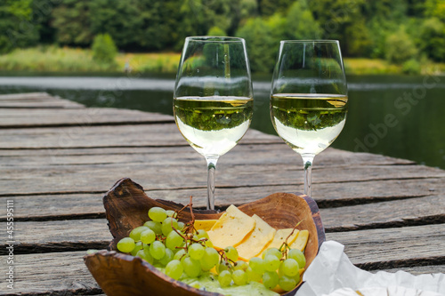 Picnic at the wooden pier by the lake with food, fruit and white wine. Picnic for two, romantic outdoor recreation
